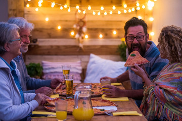 group of four people eating together at home or restaurant with pizzas and beers - funny scene of woman giving a pieze of pizza at his husband or boyfriend