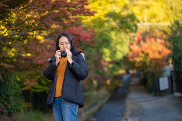 Young beautiful photographer with the professional camera taking photo beautiful autumn colourful maple leaf in Kyoto Japan.