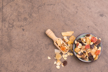 Muesli with dried fruits in a bowl on a brown textured background, empty copy space, healthy breakfast