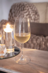 Wine glass on wooden table in living room, cosy sofa and warm blanket in the back. Relax at home concept.