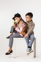 Cute stylish little couple child boy and happy girl with white rose sittting together at studio. kids fashion concept.