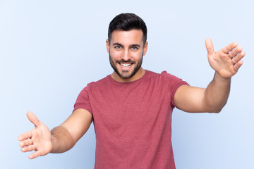 Fototapeta premium Young handsome man with beard over isolated blue background presenting and inviting to come with hand