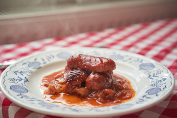 Close up Picture of typical czech beer specialty served in pubs. Roasted small sausages in spicy beer sauce consist from dark beer, tomatoes, chili, garlic and onion ans served with beer and bread.