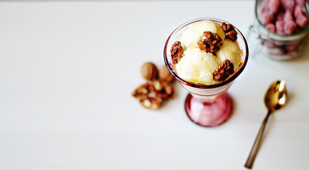 Creamy ice cream with honey and walnuts. Served in a bowl with ice cream, garnished with walnuts and honey. On the table is a jar with dried strawberries, a spoon and a walnut.