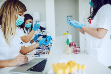 Small group of female laboratory assistants checking blood, using microscope and doing test for...