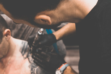Fototapeta na wymiar Tattoo salon. The tattoo master is tattooing a man on his shoulder. Tattoo machine, safety and hygiene at work. Close-up, tinted, tattooist