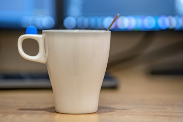 White cup of coffee or tea on blurred background of personal computer screen.