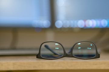 Closeup of protective glasses on an empty desk with blurred computer screen on background.