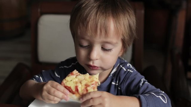 Close up of little cute boy eating pizza. Neutral colors for collor correction.