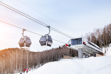 Upper passenger disembarkation point of a gondola cableway with a booth suspended on a rope on a background of mountains on winter sunset. Ski resorts and snowboarding. © Aleksandr Kondratov
