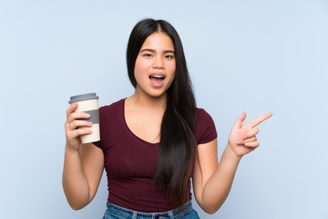 Young teenager Asian girl holding a take away coffee surprised and pointing finger to the side