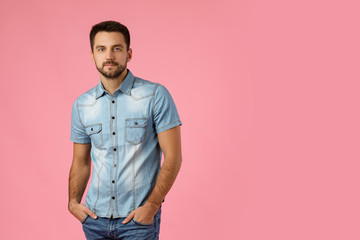 Handsome young bearded man wearing casual jeans standing against pink background. space for text