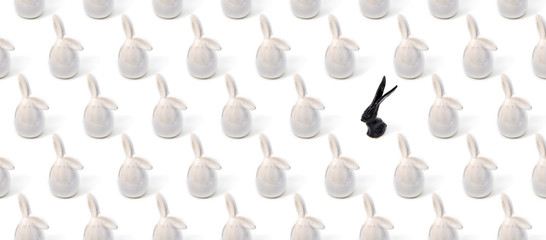 Trendy Easter pattern made of white bunny hares toys and  one black bunny on white isometric background in minimal style. Easter bunny concept, banner