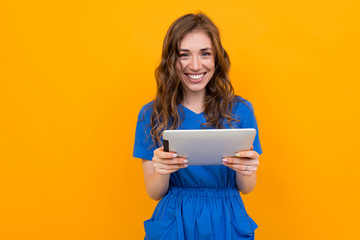 charming smiling girl in a blue dress holds a tablet on a yellow background