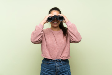 Young teenager Asian girl over isolated green background with black binoculars