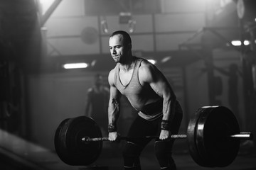 Fototapeta na wymiar Black and white photo of sportsman exercising with barbell in a gym.