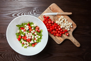 Cherry tomatoes with salad cheese on cutting board on wooden table, top view. Cooking vegetable salad
