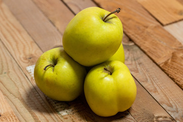 Green apples stacked on each other on a wooden counter top in front of the window cascading bright light from outside over the apples making them shine