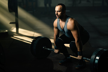Fototapeta na wymiar Muscular build man performing deadlift while having weight training in a gym.