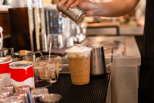 Barista sprinkles cocoa powder on iced chocolate in cafe.