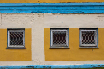 Three windows with bars of an old industrial building. Brick wall painted in yellow and blue.