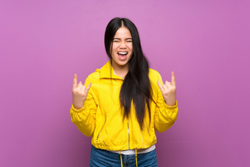 Young teenager Asian girl over isolated purple background making rock gesture