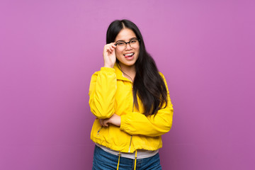 Naklejka premium Young teenager Asian girl over isolated purple background with glasses and happy