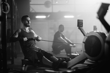 Athletic man exercising on rowing machine during sport training n a gym.