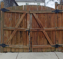 Rear view of wooden fence gate with sidewalk in foreground.