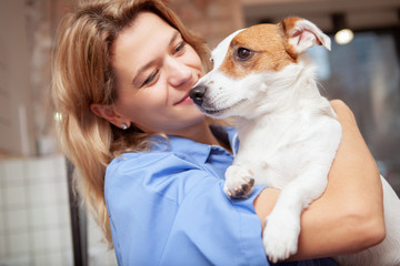 Mature female veterinarian cuddling with adorable jack russel terrier puppy. Cute dog in the arms of a friendly vet doctor
