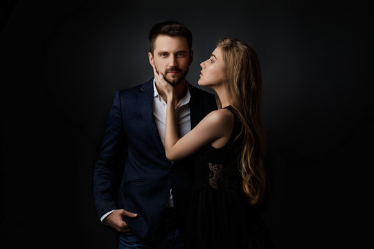 elegant couple on black background. beautiful woman in dress embracing bearded man in suit