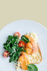 Salted salmon on toast with spinach and tomato salad served on a white plate