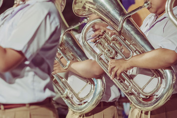 Male student with friends blow the euphonium with the band for performance on stage at night.