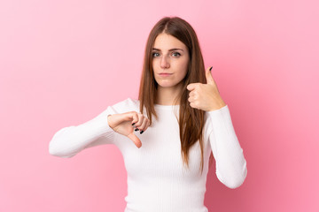 Young woman over isolated pink background making good-bad sign. Undecided between yes or not
