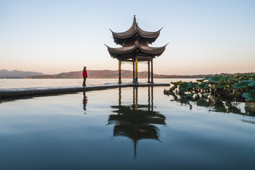 Fototapeta premium Sunrise panoramic view of the West Lake in Hangzhou, China. Girl silhouette in sunrise colors.