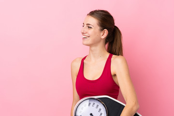 Young sport woman over isolated pink background with weighing machine