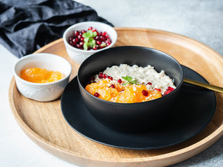 Oatmeal with fresh tangerine slices and pomegranate seeds, ground almonds and mint in a black bowl on wood round tray