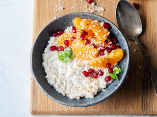 Oatmeal with fresh tangerine slices and pomegranate seeds, ground almonds and mint in a blue bowl on wood board.
