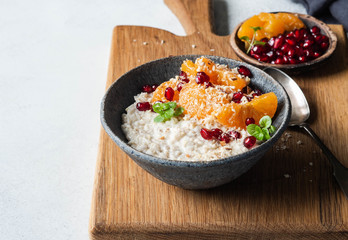 Oatmeal with fresh tangerine slices and pomegranate seeds, ground almonds and mint in a blue bowl on wood board. Copy space.