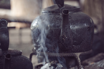 Black teapot warming up on the wooden fire