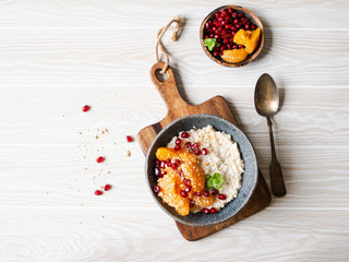 Oatmeal with fresh tangerine slices and pomegranate seeds, ground almonds and mint in a blue bowl on white background. Copy space. Top view
