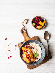 Oatmeal with fresh tangerine slices and pomegranate seeds, ground almonds and mint in a blue bowl on white background. Copy space. Top view