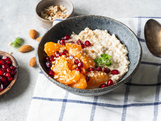 Oatmeal with fresh tangerine slices and pomegranate seeds, ground almonds and mint in a blue bowl on white background. Copy space. Top view