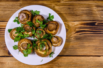 Plate with baked champignons, dill and parsley on a wooden table. Top view