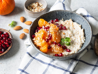 Oatmeal with fresh tangerine slices and pomegranate seeds, ground almonds and mint in a blue bowl on white background. Copy space. Top view