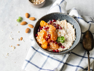 Oatmeal with fresh tangerine slices and pomegranate seeds, ground almonds and mint in a blue bowl on white background.