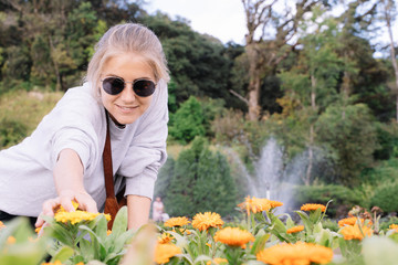 Naklejka na ściany i meble Blonde girl smiling with sunglasses holding some yellow carnations with a jet of water coming out