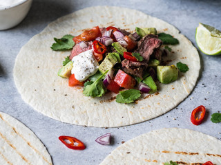Tortillas with vegetables and beef steak slices. Avocados, tomatoes, red onions and meet with cilantro and lime juice in tortillas. Mexican food.