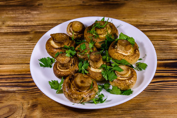 Plate with baked champignons, dill and parsley on a wooden table