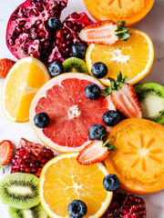 Multicolored seasonal healthy natural fruit composition with persimmon, blueberries, orange, kiwi, strawberries, grapefruit, pomegranate, orange slices.